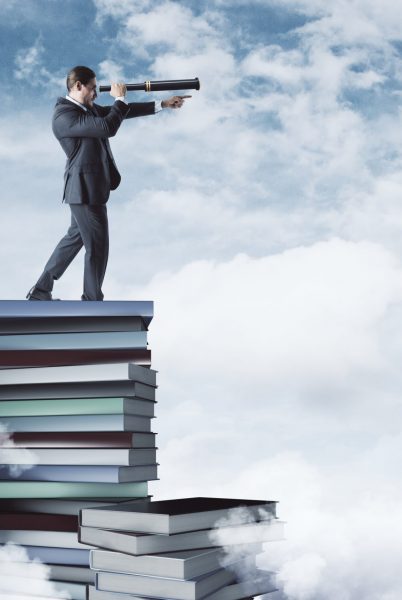 Curios businessman standing on book pile on cloudy sky and city background. Vision and education concept